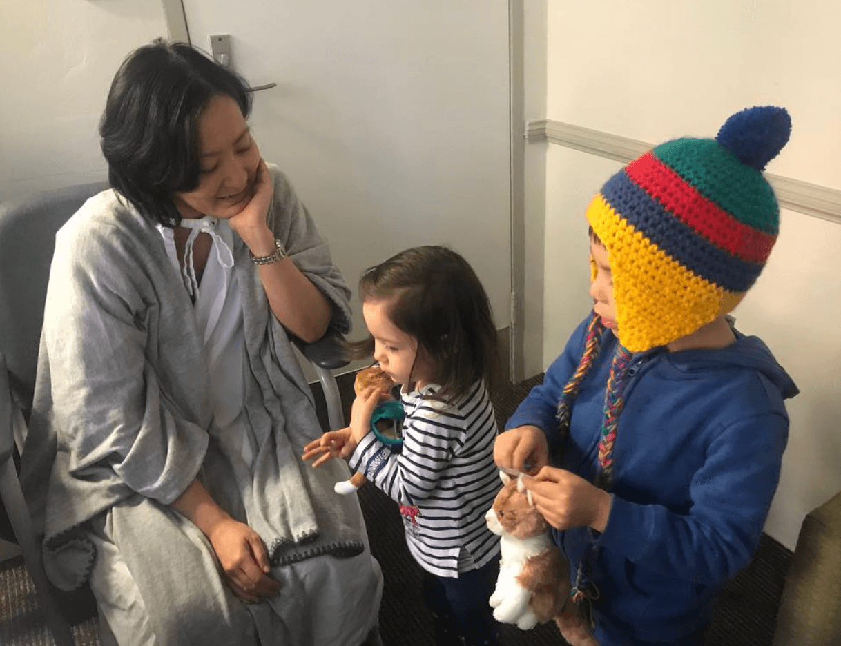 Katrina Lau Hammond wearing a cardigan and hospital gown. She looks at her son and daughter.