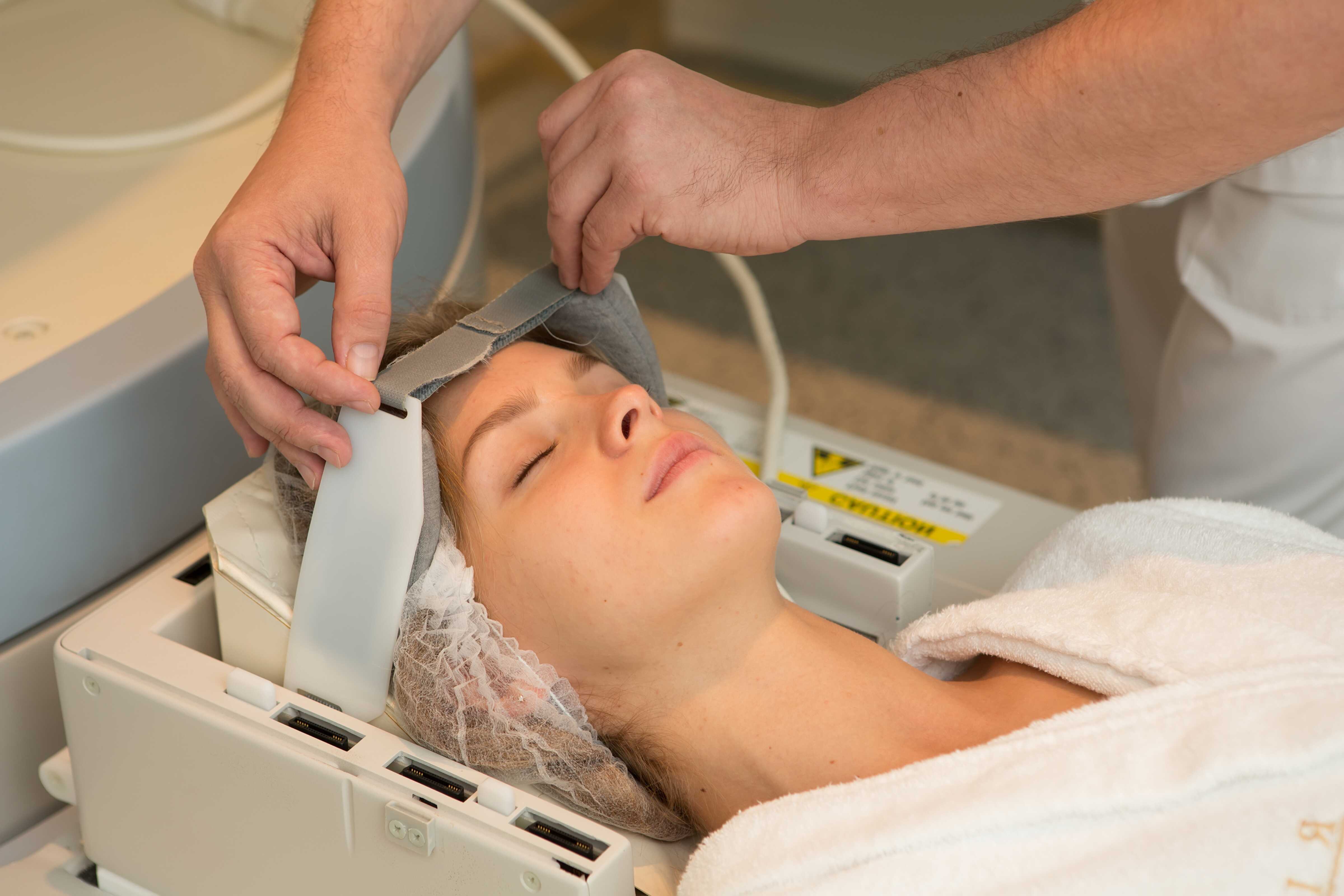 A clinician examines a woman wearing a cap and robe for magnetic resonance imaging.