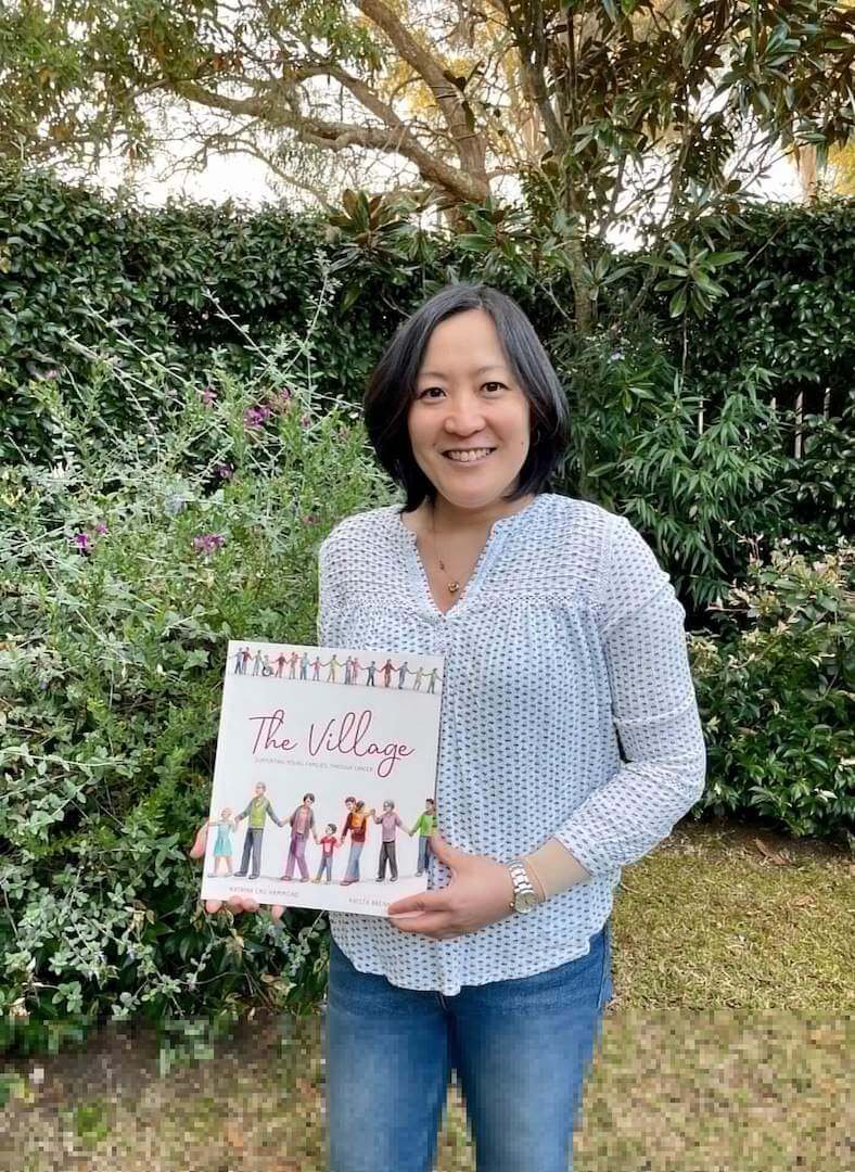 Katrina Lau Hammond is smiling and holding her picture book 'The Village'